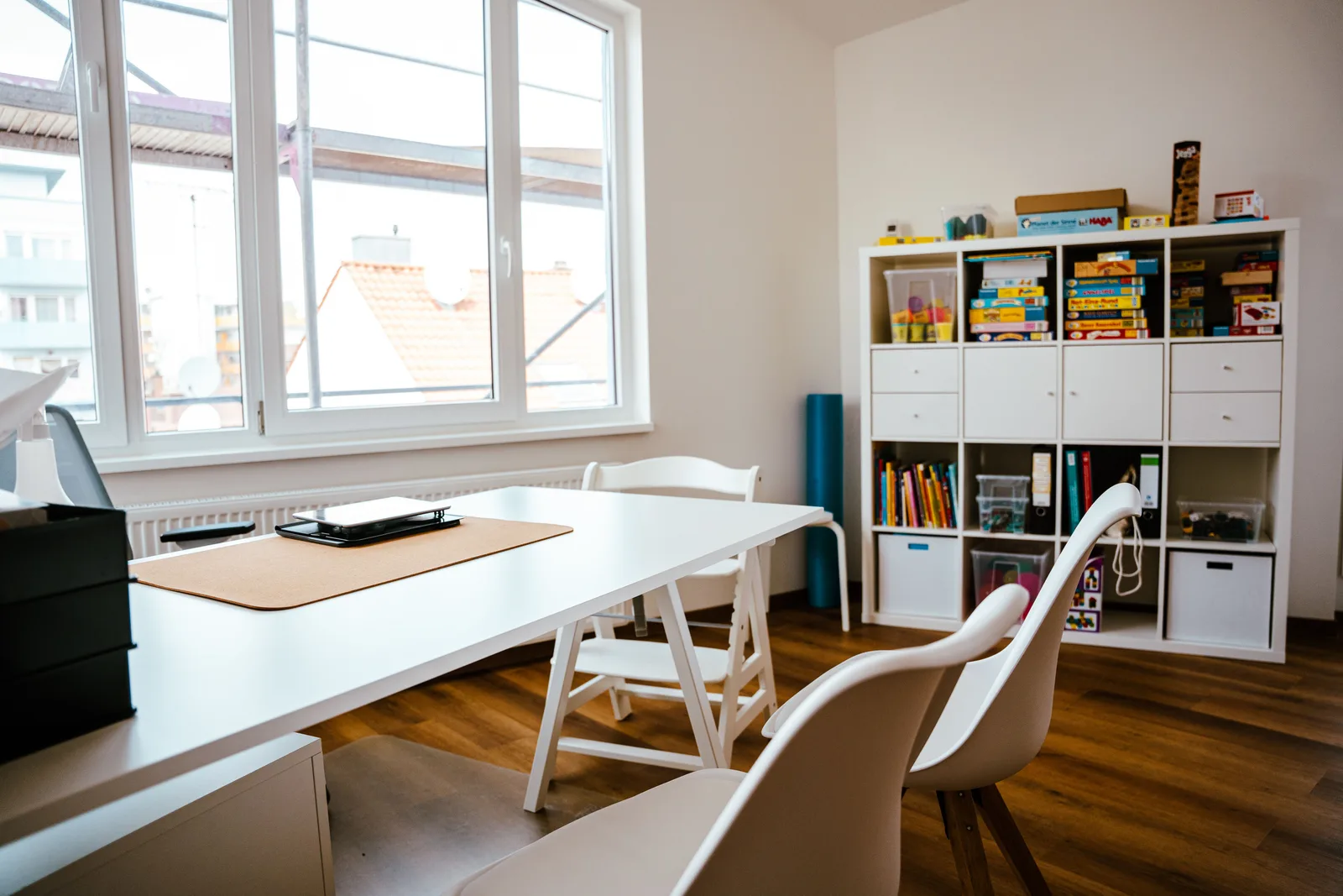 Langer Arbeitstisch am Fenster, dahinter ein Regal mit Ordnern und Fachliteratur