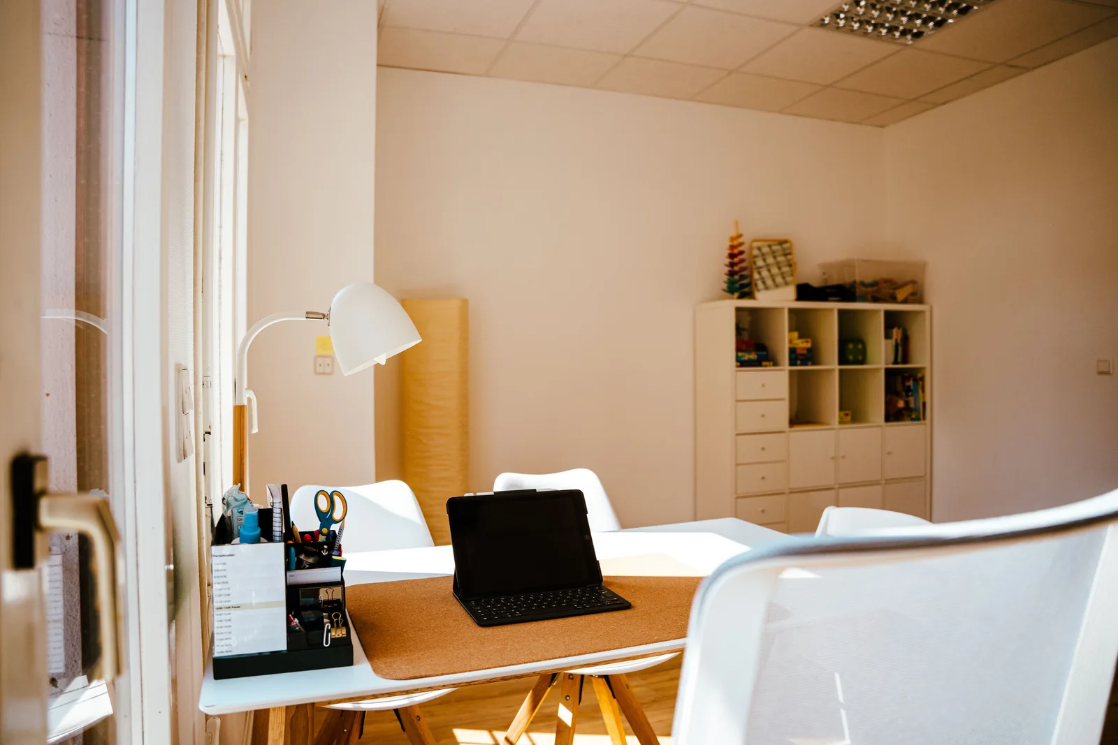 Arbeitsplatz mit Laptop, Schreibtischlampe und Materialregal in der Therapiepraxis