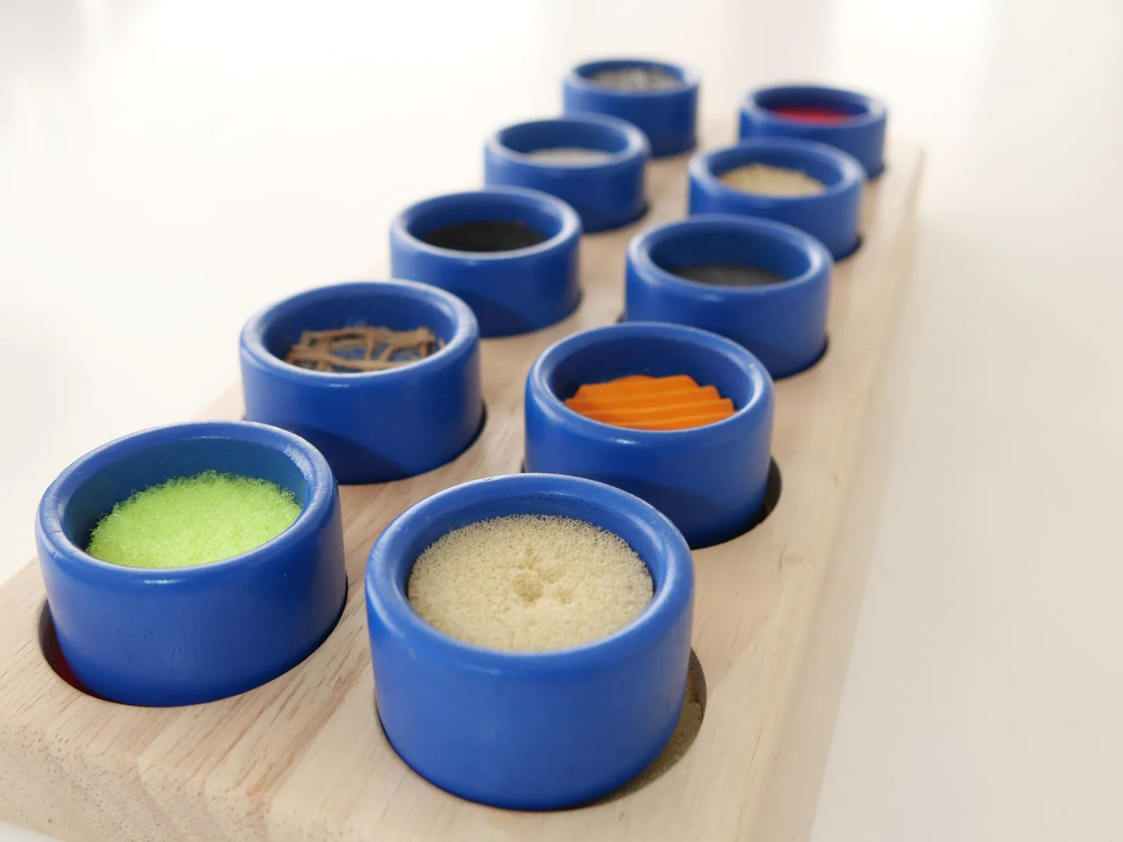 Reihe blauer Schalen mit unterschiedlichem Fühlmaterial auf einem Holztisch
