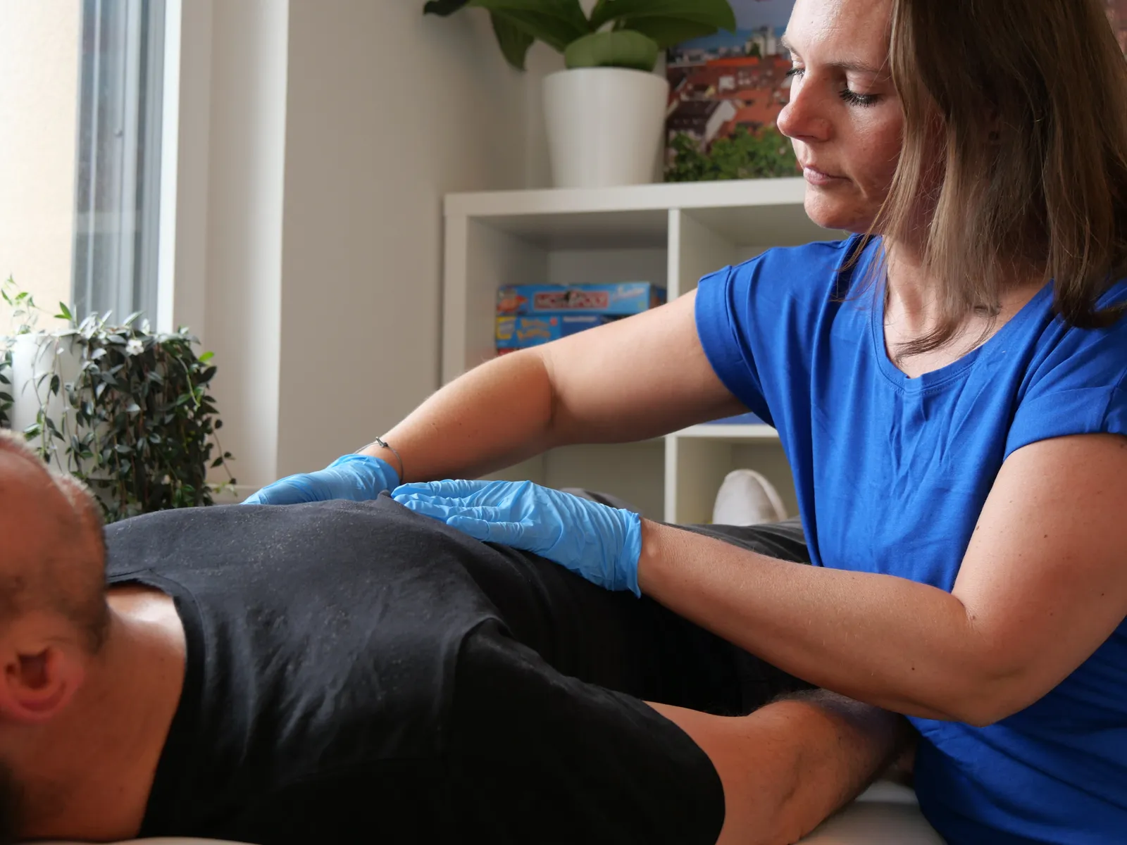 Therapeutin behandelt einen liegenden Patienten mit den Händen an der Behandlungsliege