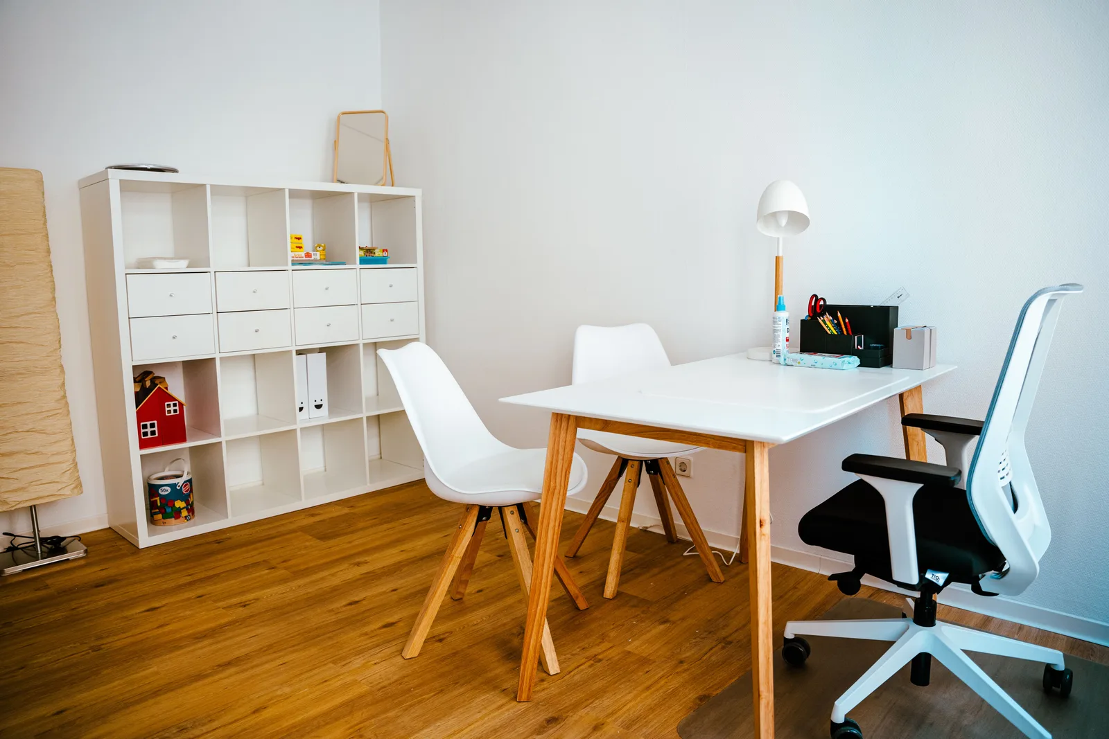 Arbeitstisch mit Stühlen vor einem offenen Materialregal in der Therapiepraxis