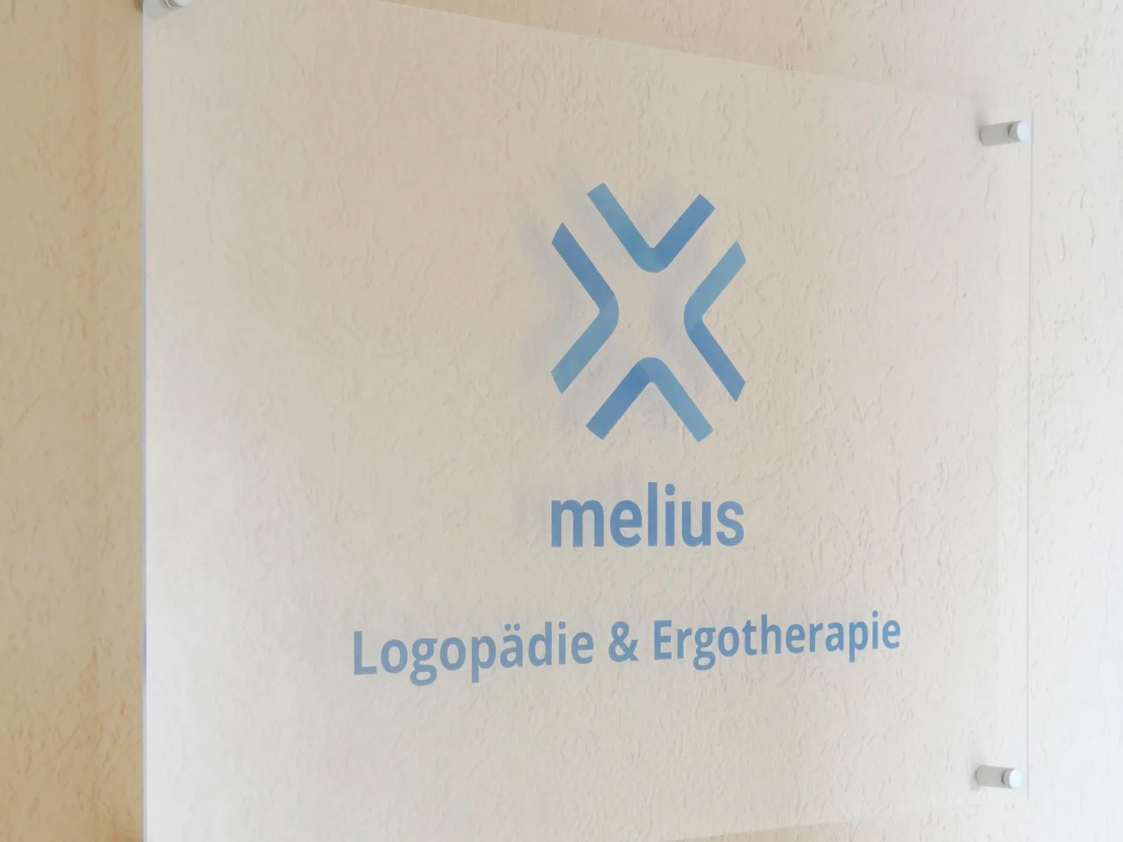 Praxisschild aus Glas mit dem melius-Logo und dem Schriftzug Logopädie und Ergotherapie