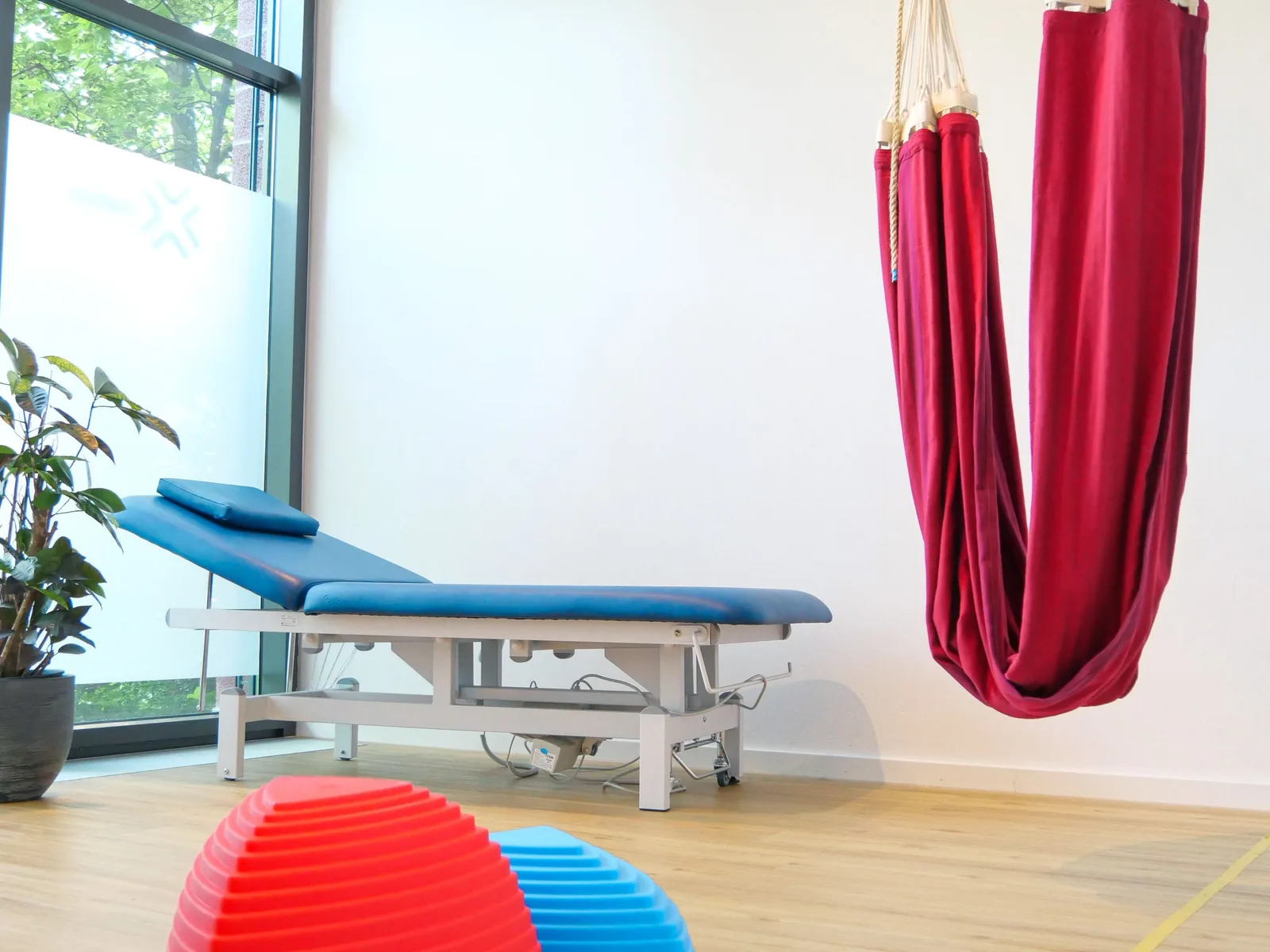 Therapieraum mit roter Hängematte, Behandlungsliege und Balancehalbkugeln